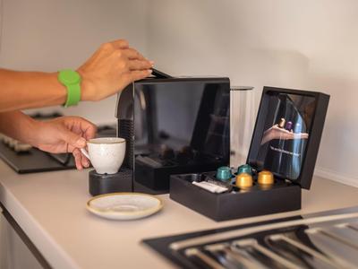 Person bereitet in einer Hotelküche Kaffee mit einer Kapselmaschine und verschiedenen Kapseln zu.
