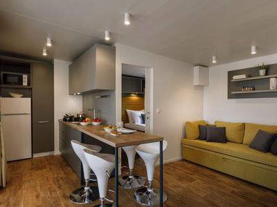 Moderne Hotelzimmerküche mit Bartheke, zwei Hockern, Sofa und Holzboden.