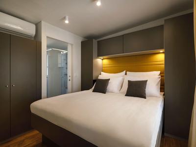 Schlafzimmer mit großem Bett, dunklen Schränken und modernem Bad, ideal für Reisen.