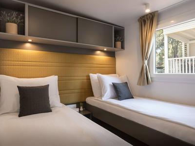 Zwei Einzelbetten mit weißen Bettwäsche und Kissen neben einem Fenster in einem Hotelzimmer.