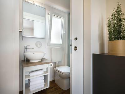 Kompaktes Badezimmer mit weißem Waschbecken, Toilette und Handtüchern unter einem Holzregal.