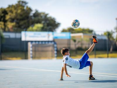 Junger Fußballspieler führt Trick auf offenem Sportplatz bei Tageslicht vor.