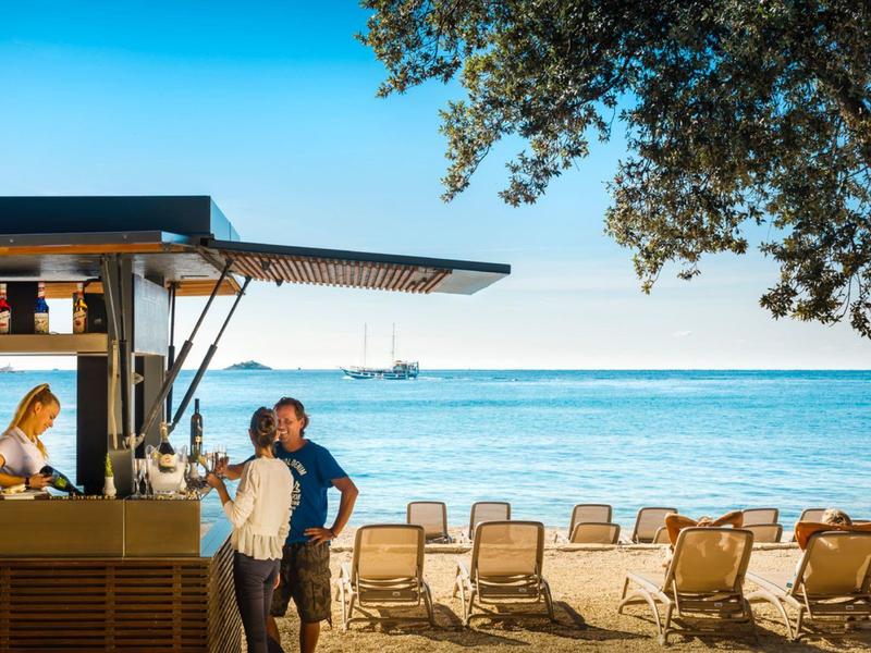 Strandbar met ligstoelen en uitzicht op zee onder een blauwe lucht.