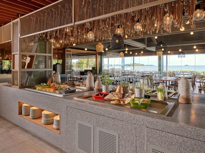 Modern buffet met geselecteerd eten en drinken in een licht restaurant met uitzicht naar buiten.
