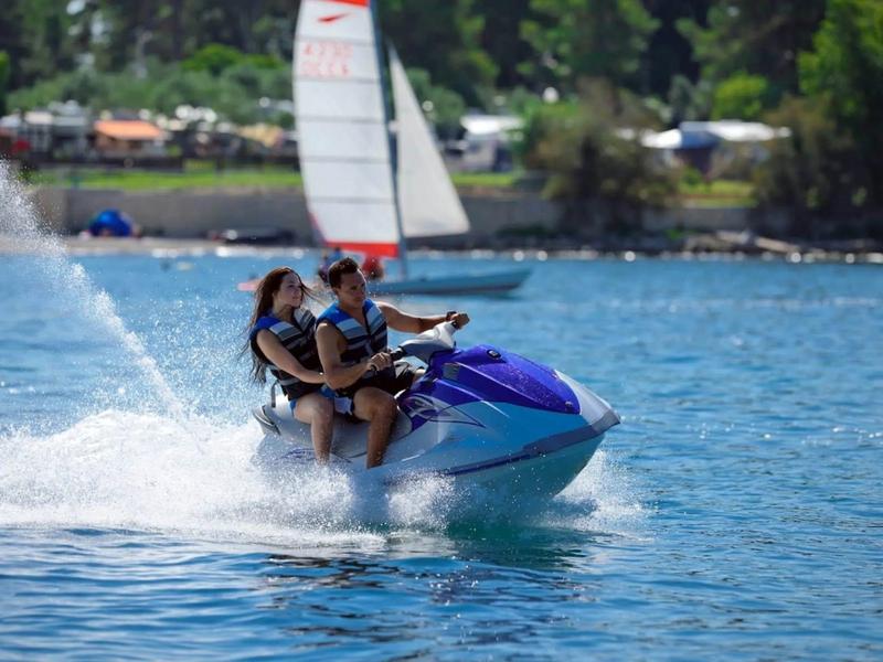 Twee mensen rijden op een jetski op een meer bij zonnig weer.