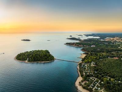 Veduta aerea di un paesaggio costiero con isola, ponte e tramonto.