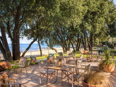 Terrazza con tavoli e sedie sotto gli alberi con vista sul mare.