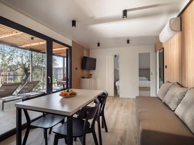 Nowoczesny salon z stołem jadalnym, krzesłami i sofą obok dużych przeszklonych okien z widokiem na taras.