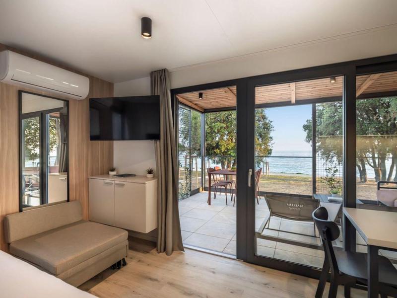 Jasny pokój hotelowy z częścią wypoczynkową i widokiem przez duże okna na taras i morze.