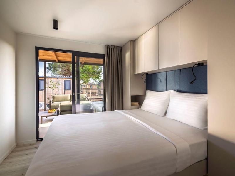 Nowoczesny pokój hotelowy z łóżkiem podwójnym i dostępem do balkonu z miejscem do siedzenia.