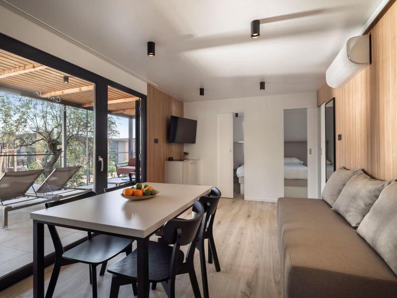 Nowoczesny salon z stołem jadalnym, krzesłami i sofą obok dużych przeszklonych okien z widokiem na taras.