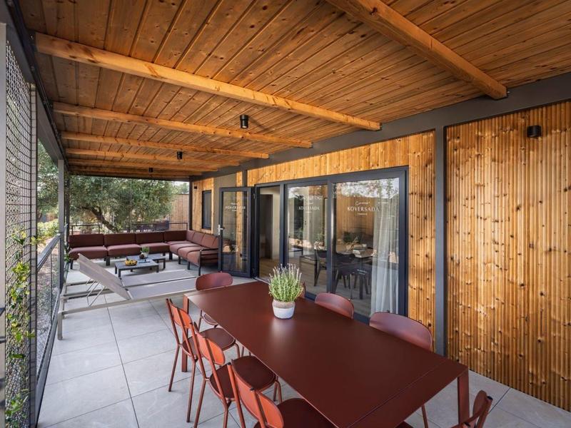 Zadaszony taras z drewnianym sufitem, długim stołem, czerwonymi krzesłami i jacuzzi.