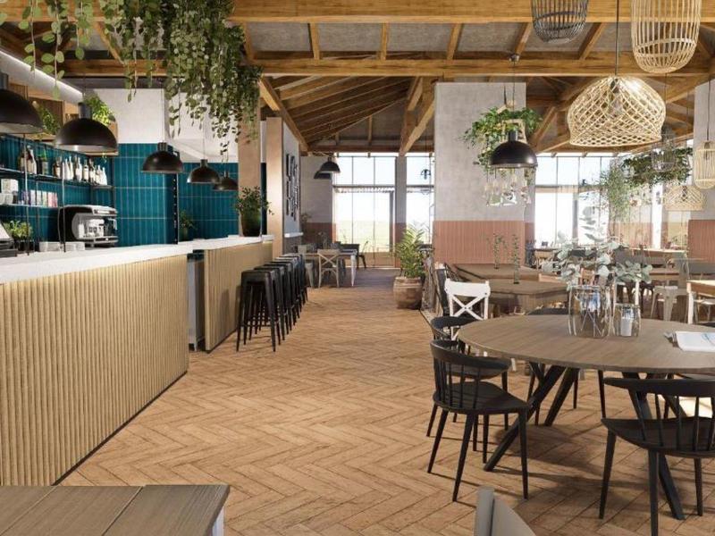 Nowoczesna restauracja z drewnianymi detalami, zielonymi kafelkami i wieloma roślinami w jasnym świetle naturalnym.