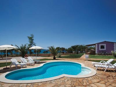 A calm pool area with umbrellas, lounge chairs, and a sea view under a clear sky.