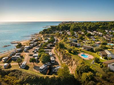 Aerial view of a coastal campsite with caravans and a pool under a blue sky.
