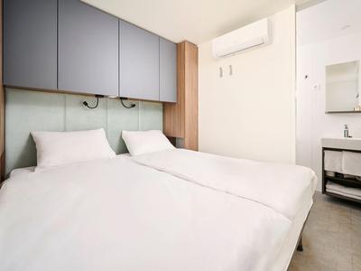 Nowoczesny pokój hotelowy z dwoma łóżkami pojedynczymi, białą pościelą i zagłówkami z lampkami do czytania.