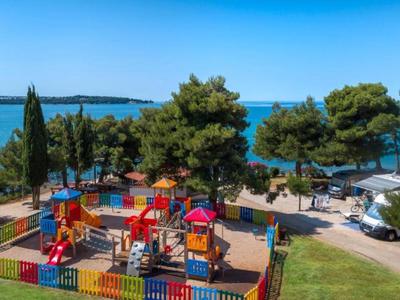 Plac zabaw z kolorowym ogrodzeniem i widokiem na morze obok kampera w parku wakacyjnym.