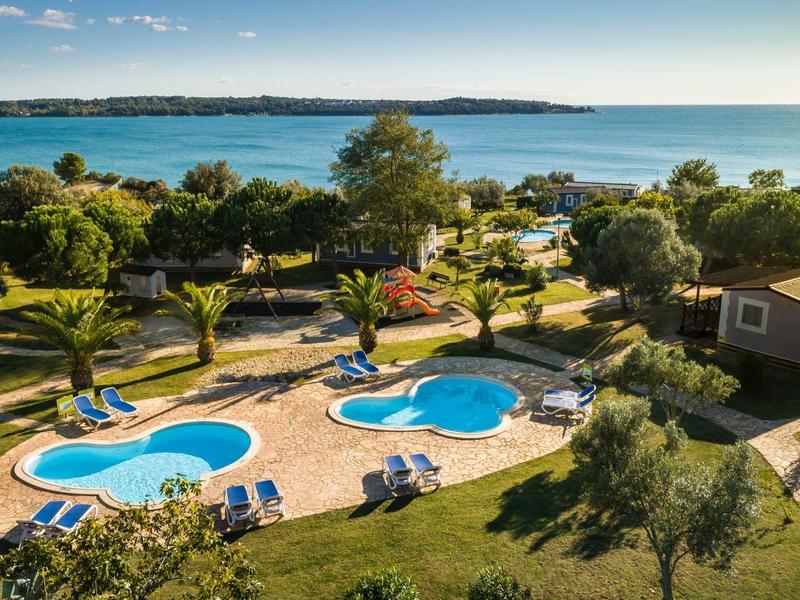 Widok na dwa baseny o unikalnych kształtach w ogrodzie z widokiem na morze o zachodzie słońca.