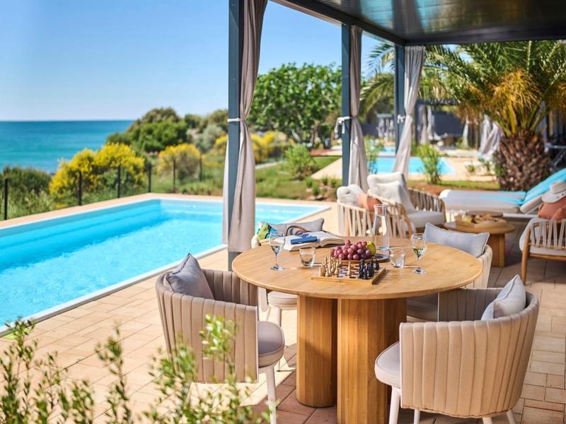 Taras z stołem, basenem i widokiem na morze w tropikalnym otoczeniu.