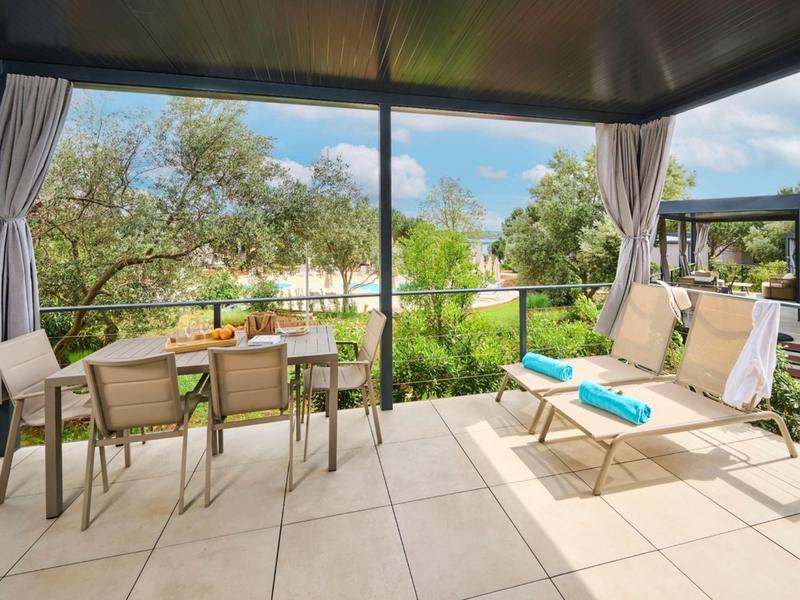 Zadaszony taras z miejscami do siedzenia i stołem z widokiem na zielony krajobraz i drzewa.