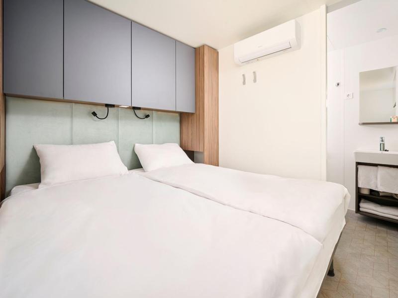 Nowoczesny pokój hotelowy z dwoma łóżkami pojedynczymi, białą pościelą i zagłówkami z lampkami do czytania.