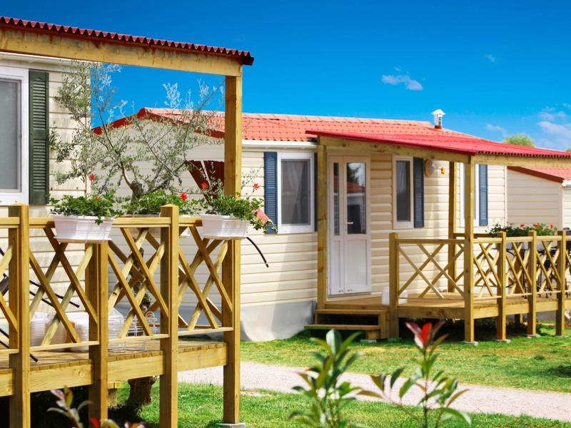 Przytulny domek mobilny z drewnianym tarasem i czerwonym dachem w słoneczny dzień.