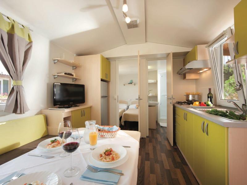 Nowocześnie urządzony salon i kuchnia z stołem jadalnym w jasnym pokoju hotelowym.