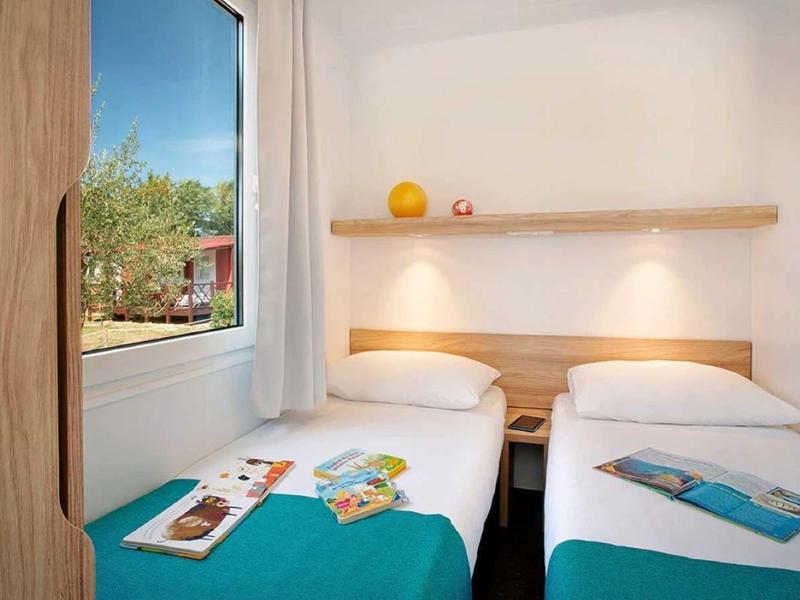 Dwa pojedyncze łóżka w jasnym pokoju hotelowym z oknem i widokiem na zieleń.