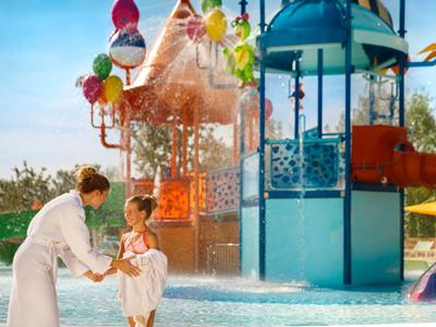 Dziecko bawi się z dorosłym na kolorowym placu zabaw wodnym w słoneczny dzień.