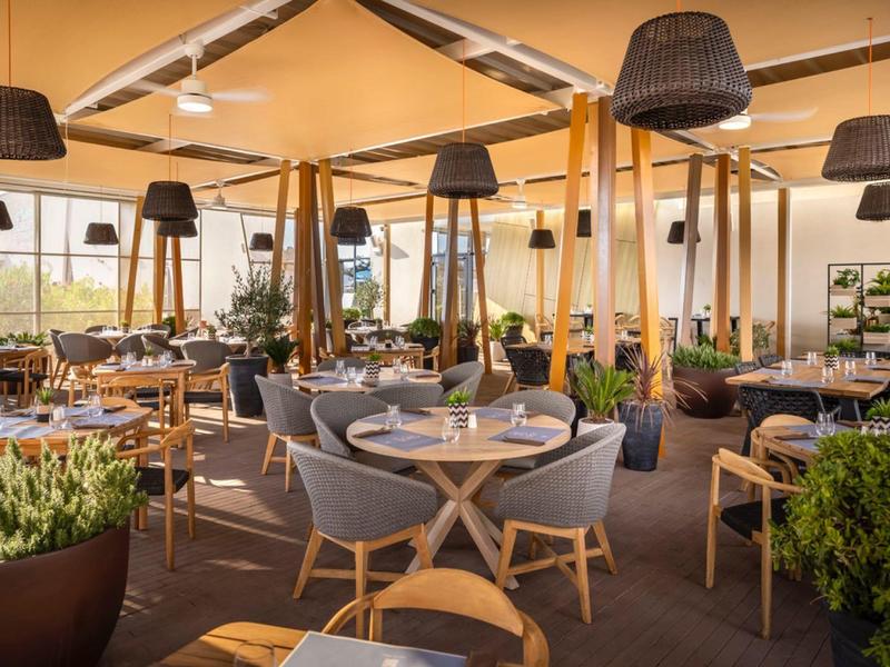 Przytulny taras restauracyjny z stołami, krzesłami i roślinami pod zadaszeniem.