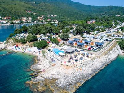 Luchtfoto van een rotsachtig strand met ligbedden en een omliggende kustplaats.