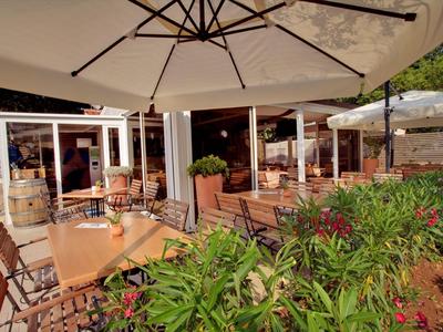 Terrazza esterna di un bar con sedie di legno, tavoli e grandi ombrelloni in una giornata di sole.