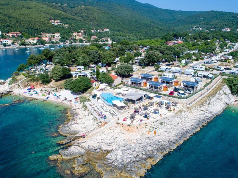 Vista aérea de una playa rocosa con tumbonas y un pueblo costero circundante.