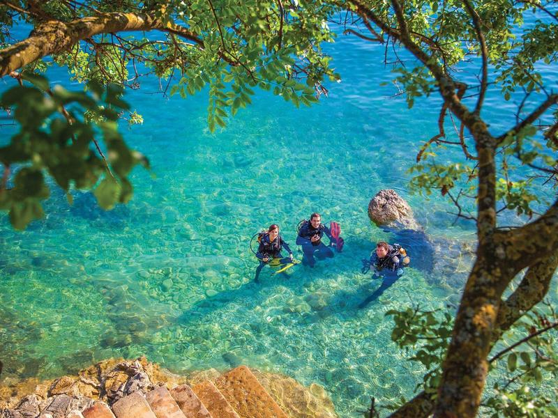 Laguna azul clara con tres esnorquelistas y rocas, enmarcada por ramas verdes.