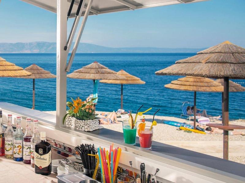 Bar en la playa con vista al mar azul y sombrillas de paja en la playa de arena.
