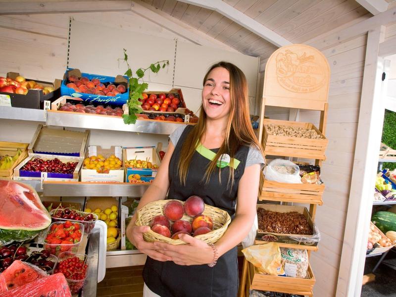 Vendedora en una tienda de frutas sosteniendo una cesta de manzanas y sonriendo.