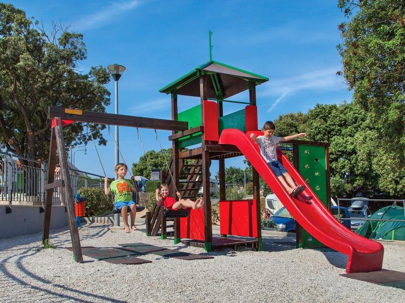 Niños jugando en un parque rojo y negro con tobogán y columpio al aire libre.