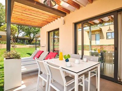 Terraza cubierta con mesa, sillas y banco cómodo con cojines en el área del jardín.