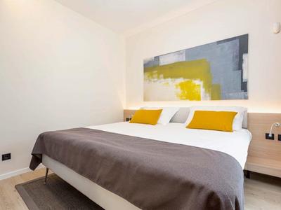 Dormitorio moderno con cama doble, cojines amarillos y obra de arte abstracta en la pared.