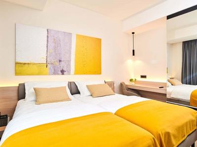 Habitación de hotel moderna con dos camas, mantas amarillas, almohadas y arte mural colorido.