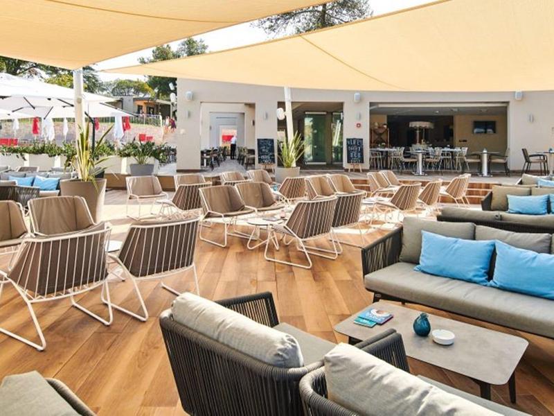 Área exterior moderna de un hotel con asientos y velas de sombra en un día soleado