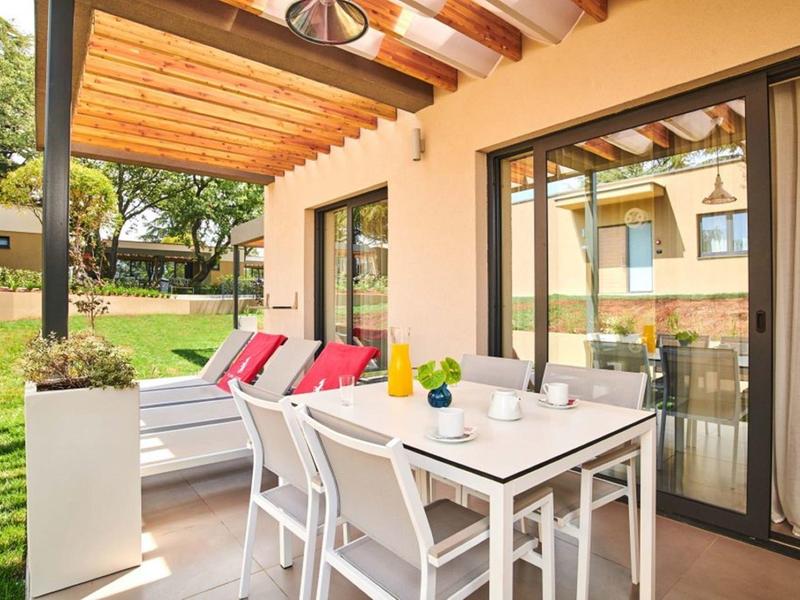 Terraza cubierta con mesa, sillas y banco cómodo con cojines en el área del jardín.