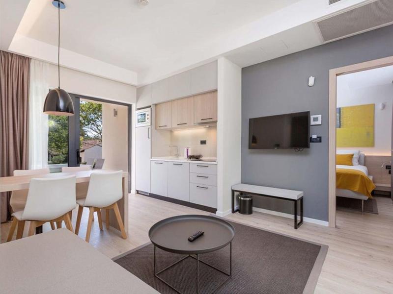 Habitación de hotel moderna con cocina, mesa de comedor, área de estar y vista al dormitorio.