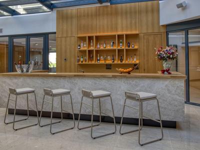 Moderner Hotelbarbereich mit vier Hockern und einem Marmor-Thekenbereich unter Tageslicht.