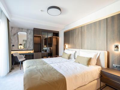 Modernes Hotelzimmer mit großem Bett, Schreibtisch und Kleiderschrank in neutralen Farben.