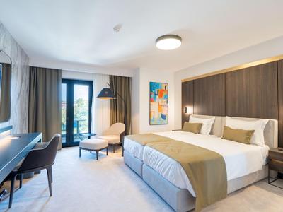 Modernes Hotelzimmer mit Doppelbett, Sessel, Schreibtisch und Blick auf den Balkon.