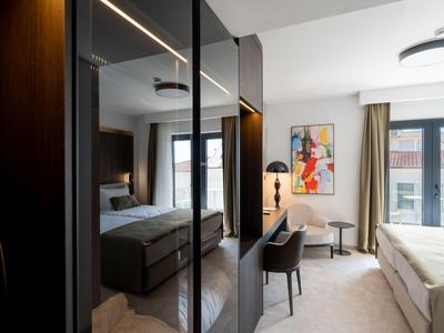 Helles Hotelzimmer mit dunklem Schrank, Bett und Schreibtisch unter moderner Beleuchtung.