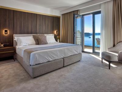Modernes Hotelzimmer mit großem Bett, Nachttischen, Stuhl und Meerblick durch Glasschiebetür.