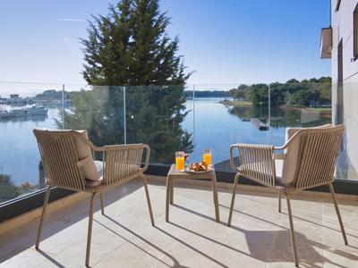 Balkon mit zwei Stühlen und Tisch mit Getränken, Blick auf einen See und Boote bei klarem Himmel.
