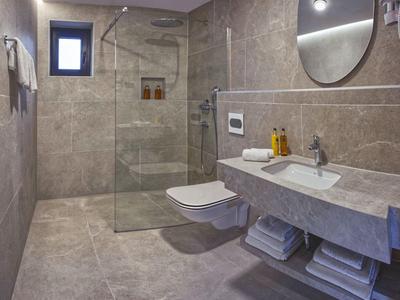 Modernes Badezimmer mit grauen Fliesen, großer Dusche und Waschbecken am Hotelzimmer.